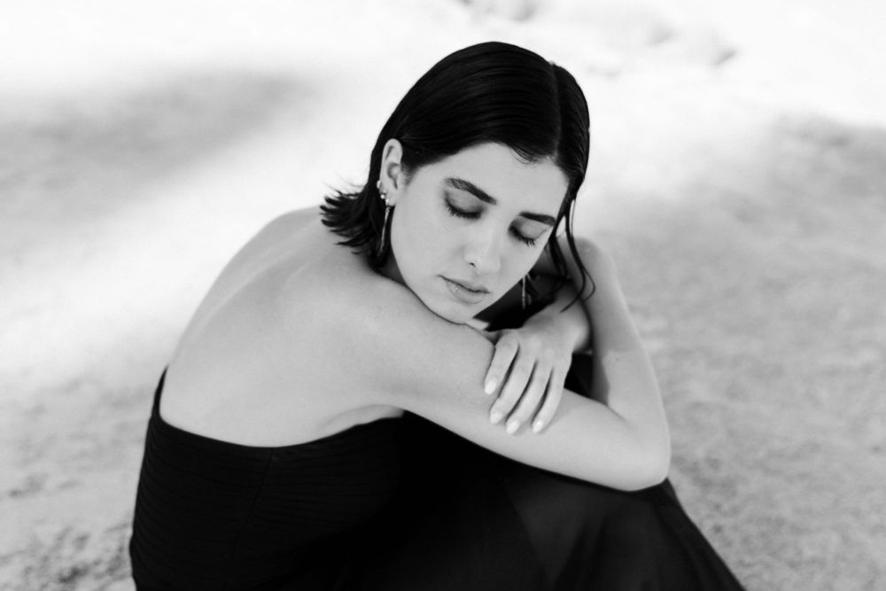 A moody black and white portrait of someone in a black dress resting against their knee.