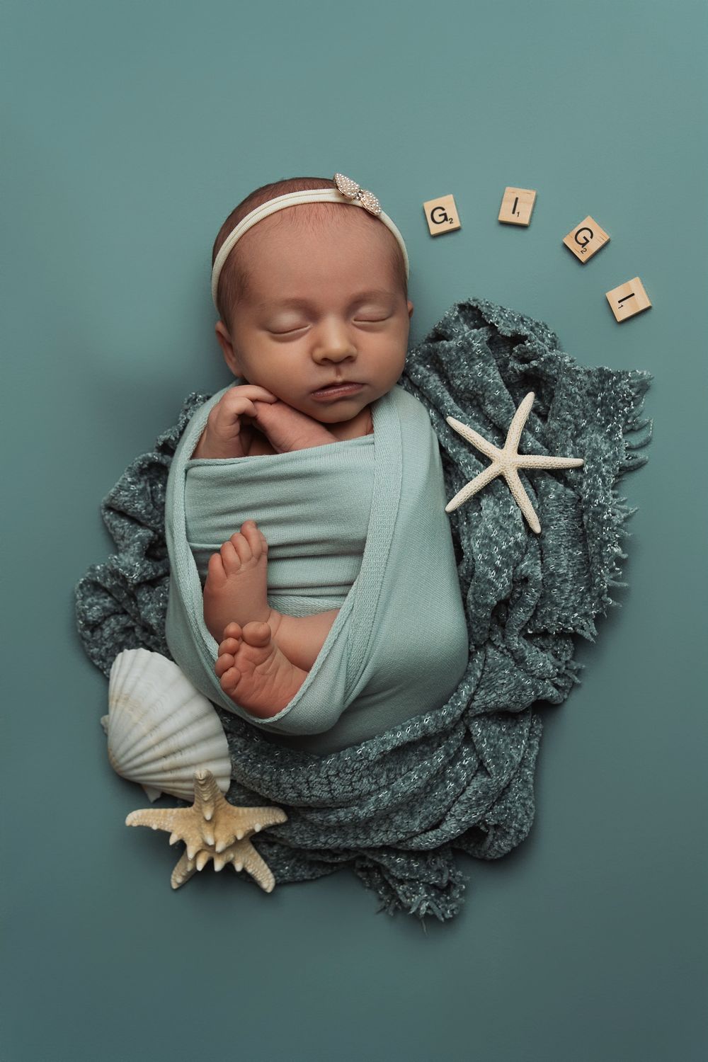 Newborn wrapped in mint fabric with nautical props and wooden blocks on teal background.