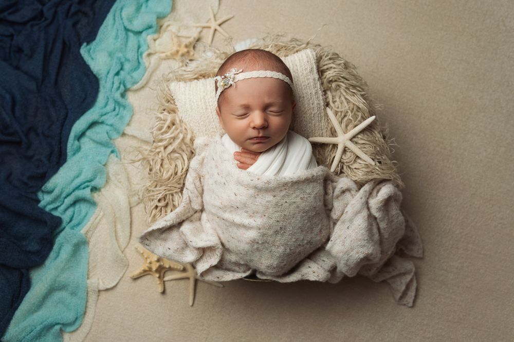 Sleeping newborn in gray wrap with coastal decor and turquoise accents in studio setting.