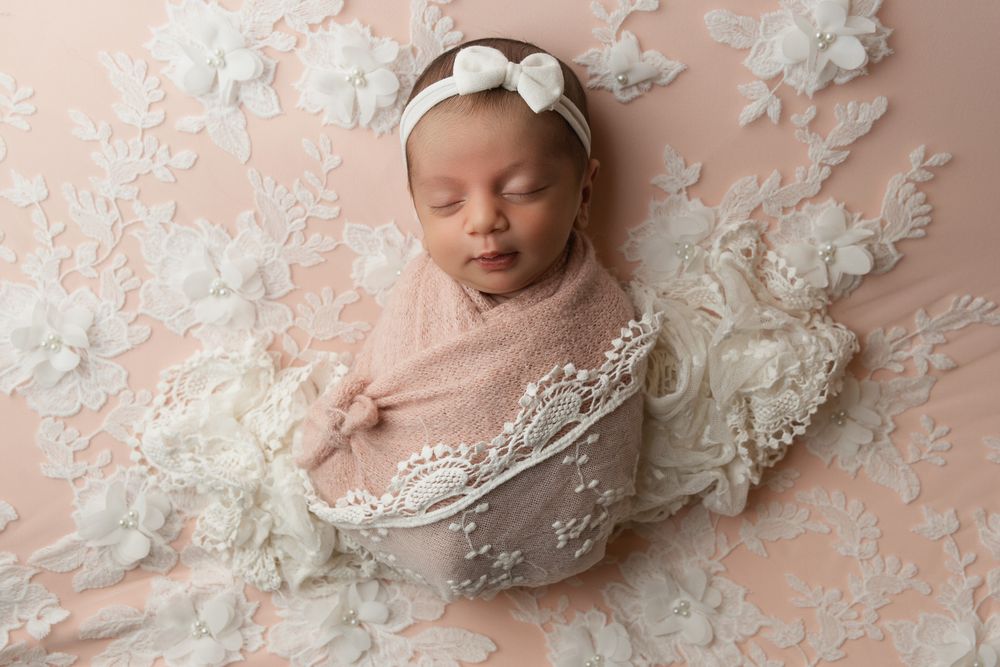 Newborn photography with white lace details and soft pink background in professional studio setting.