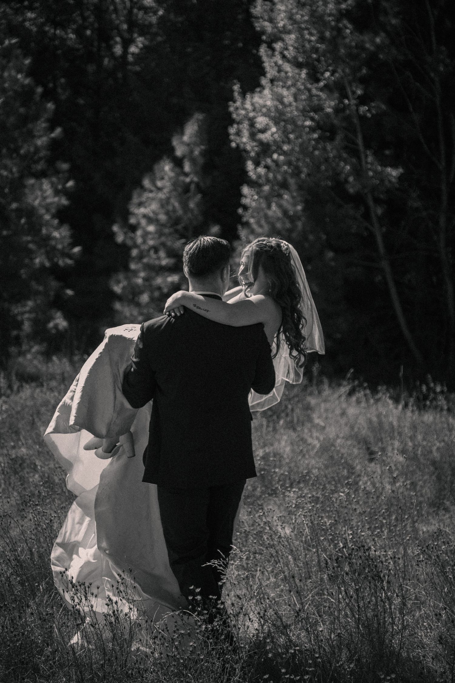 Playful embrace in a golden meadow with mountain scenery at dusk.