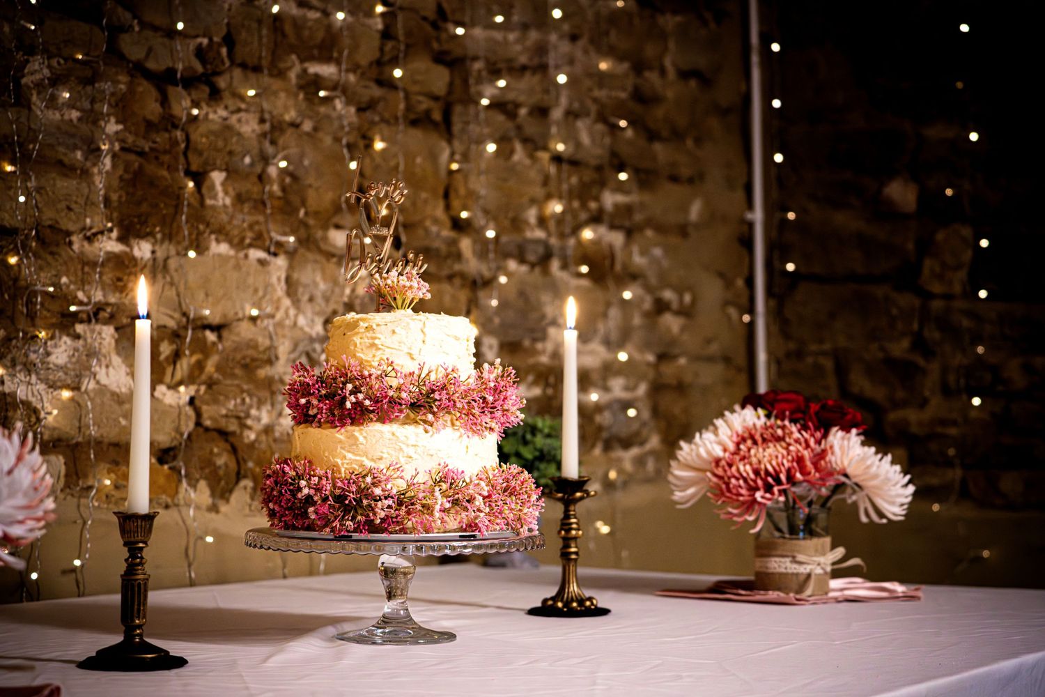 Wedding cake display on an elegant table with candlesticks in a rustic setting.
