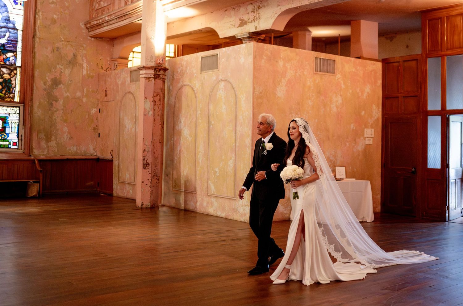 Wedding couple poses in an elegant vintage room with peach-colored walls and hardwood floors.