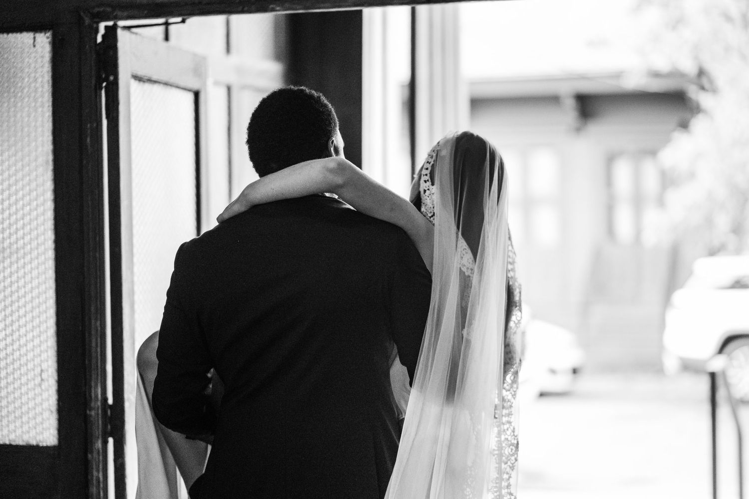 A bride and groom stand together in a doorway silhouetted in black and white on their wedding day.