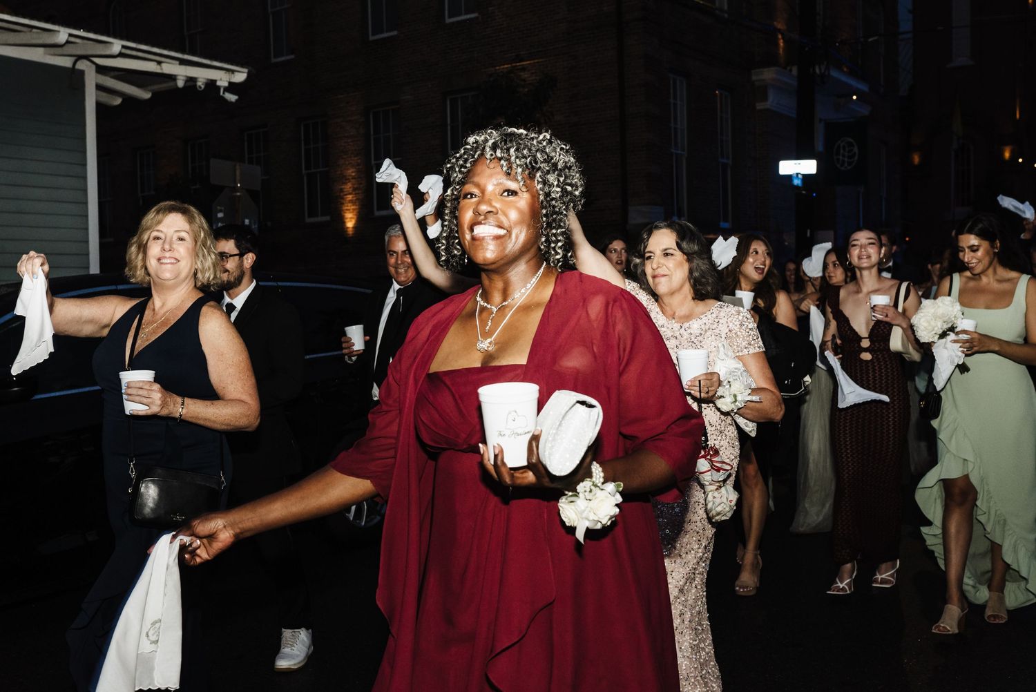A celebratory party scene with guests dancing and holding drinks while enjoying a festive evening atmosphere.