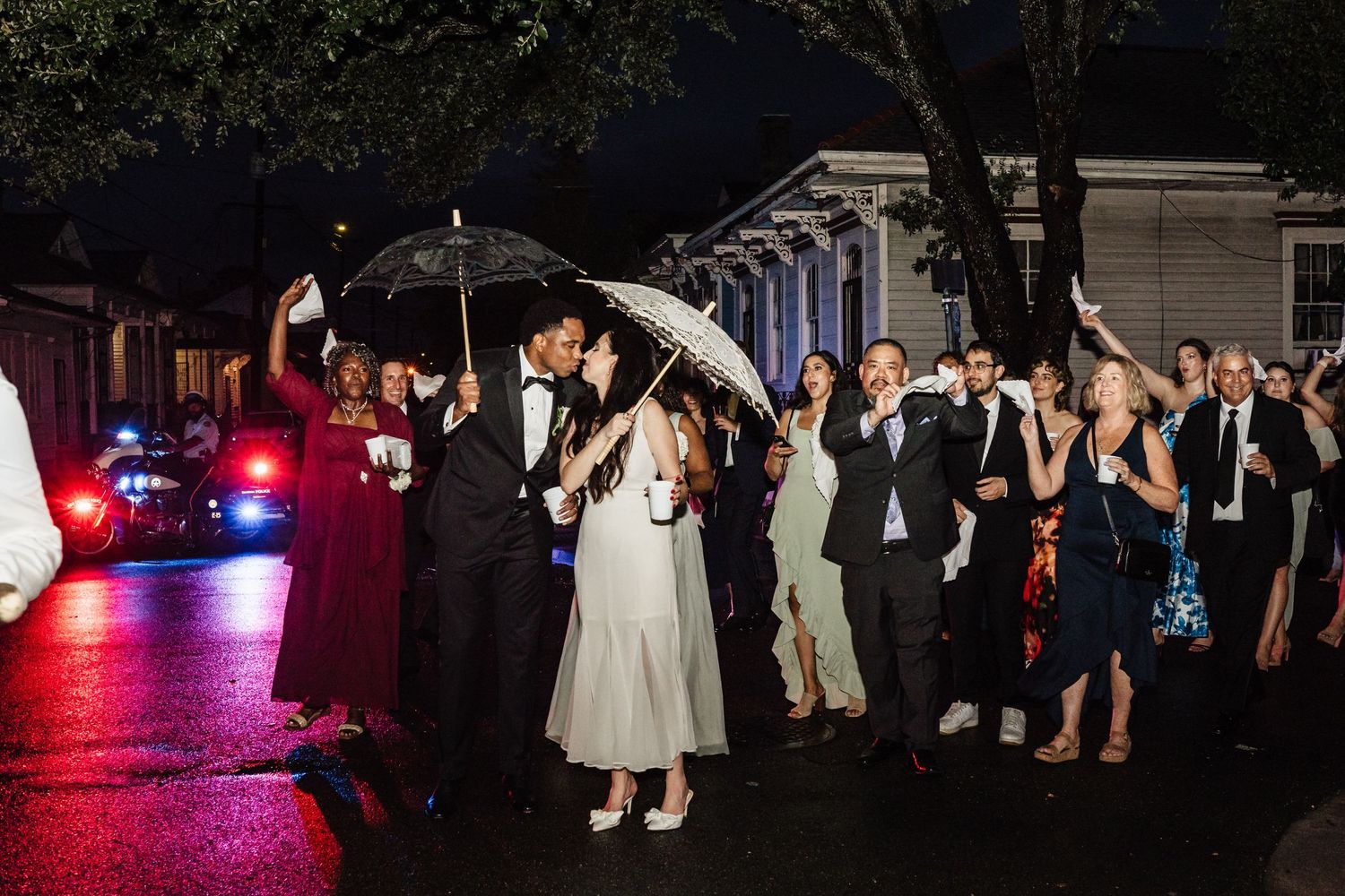 A couple dances under umbrellas at a nighttime wedding reception with red lighting and guests watching.