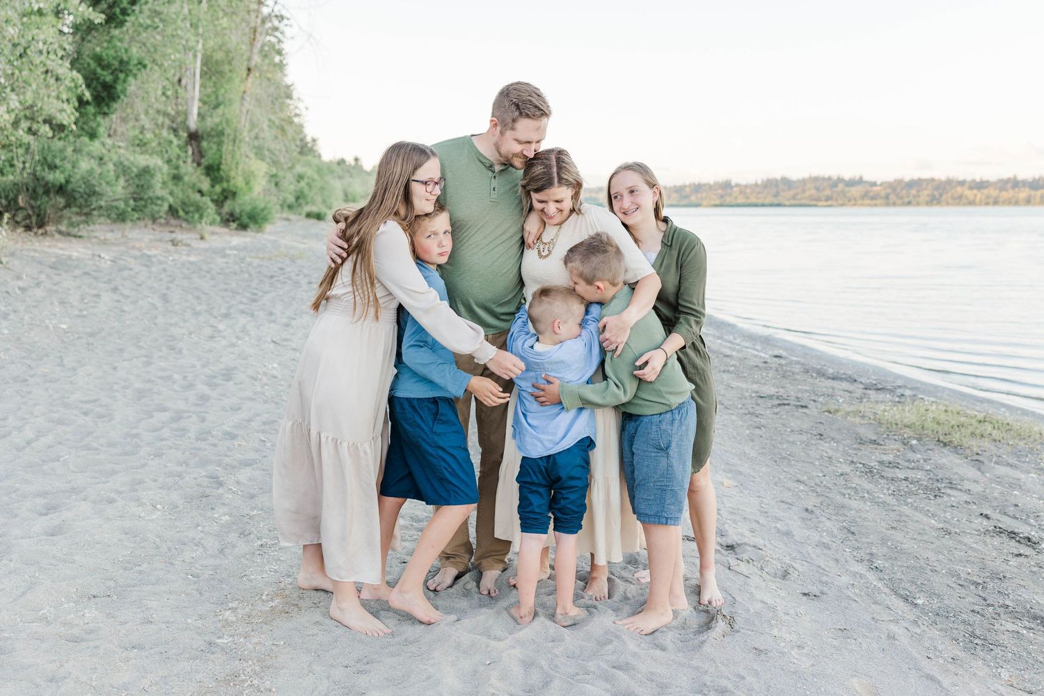 Large family group hugging together on a sandy beach shore at golden hour.