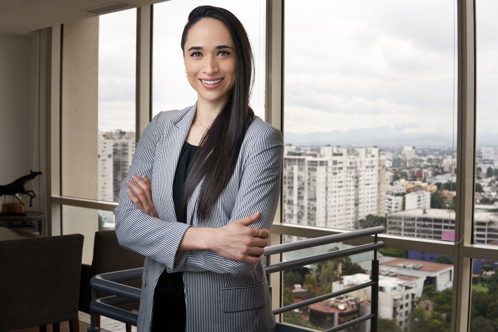 Mujer de negocios con brazos cruzados frente a ventanal con vista panorámica de la Ciudad de México.