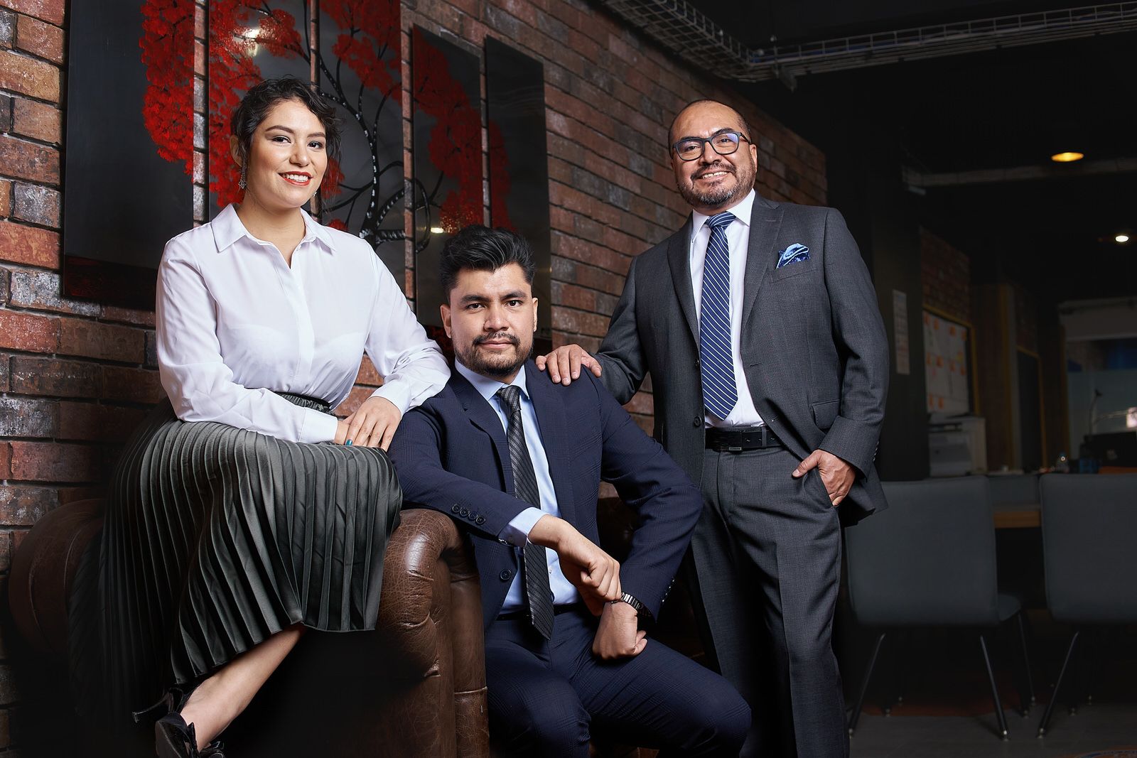 Fotografía grupal de equipo de socios sentados en sofá de piel en oficina con estilo industrial y ladrillo.