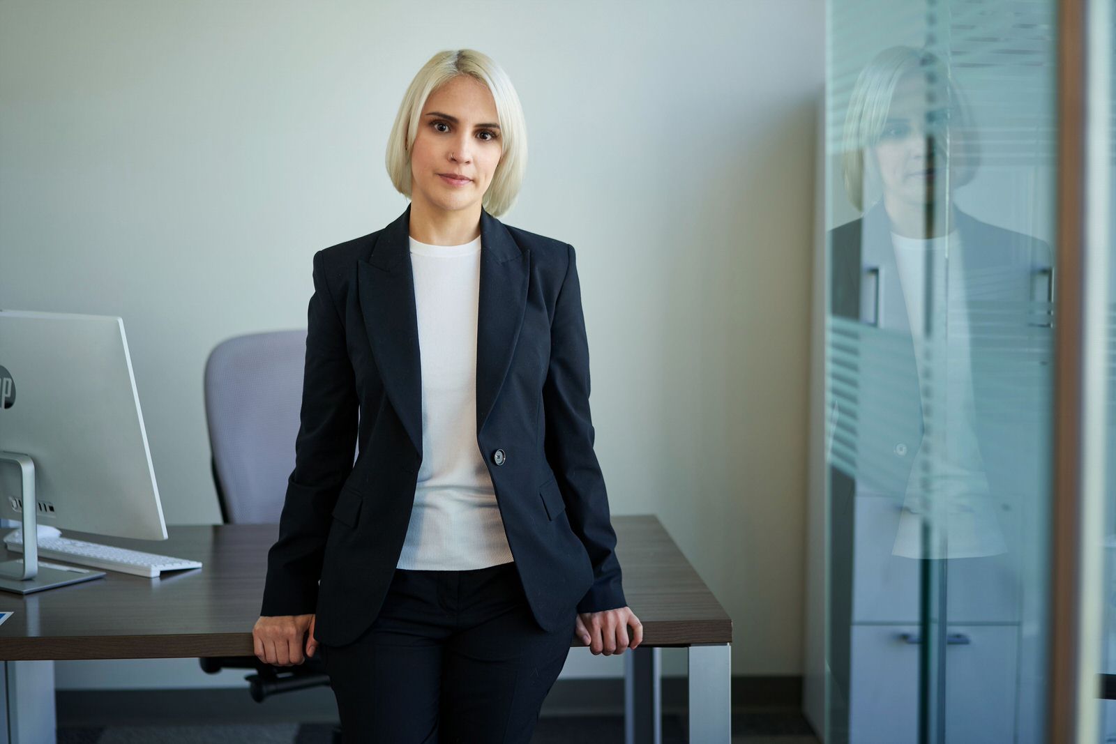 Fotografía corporativa de mujer ejecutiva rubia apoyada en su escritorio en oficina minimalista limpia.