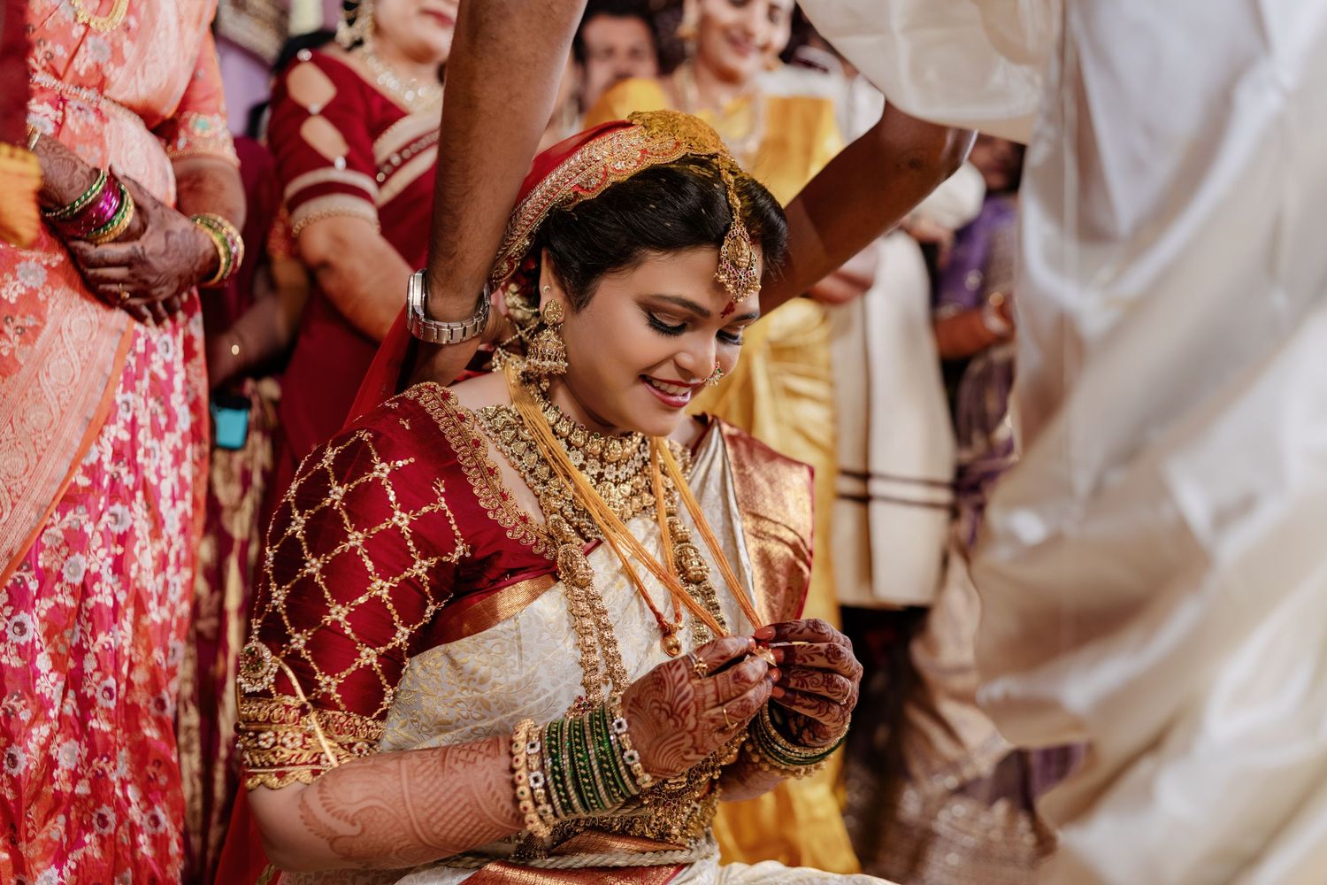 Close-up of traditional bridal jewelry and henna decorated hands with red and gold silk saree.