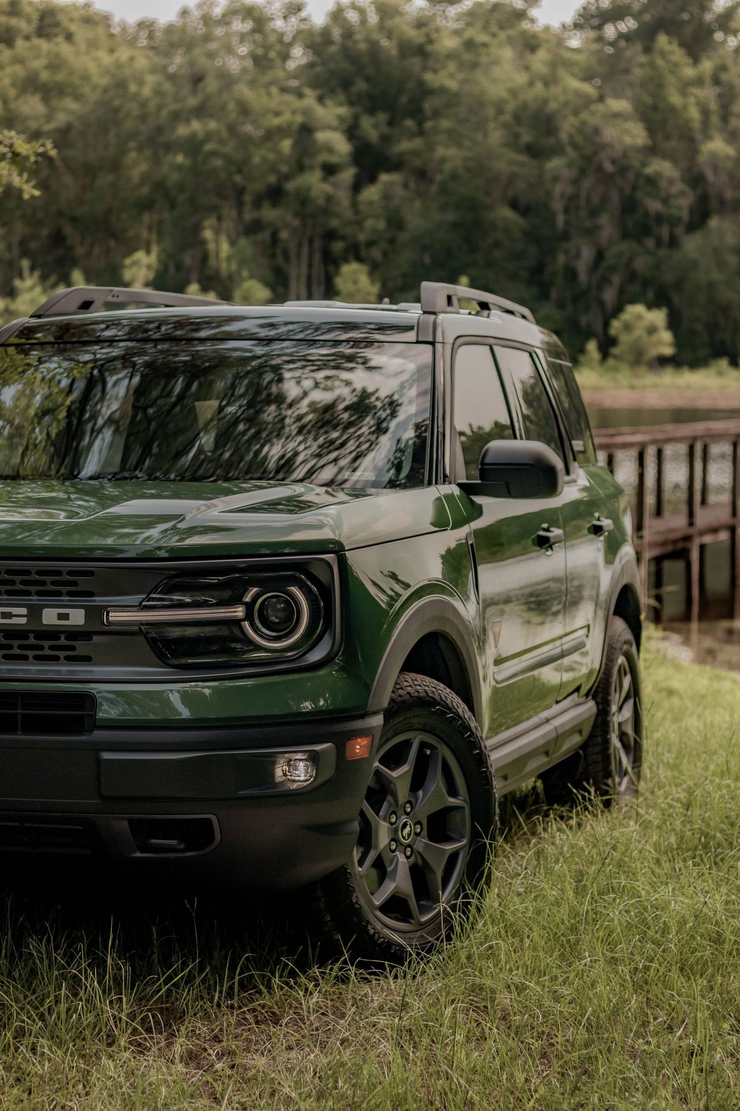 Modern green Ford Bronco Sport SUV with rugged tires parked on grassy terrain near a forest.