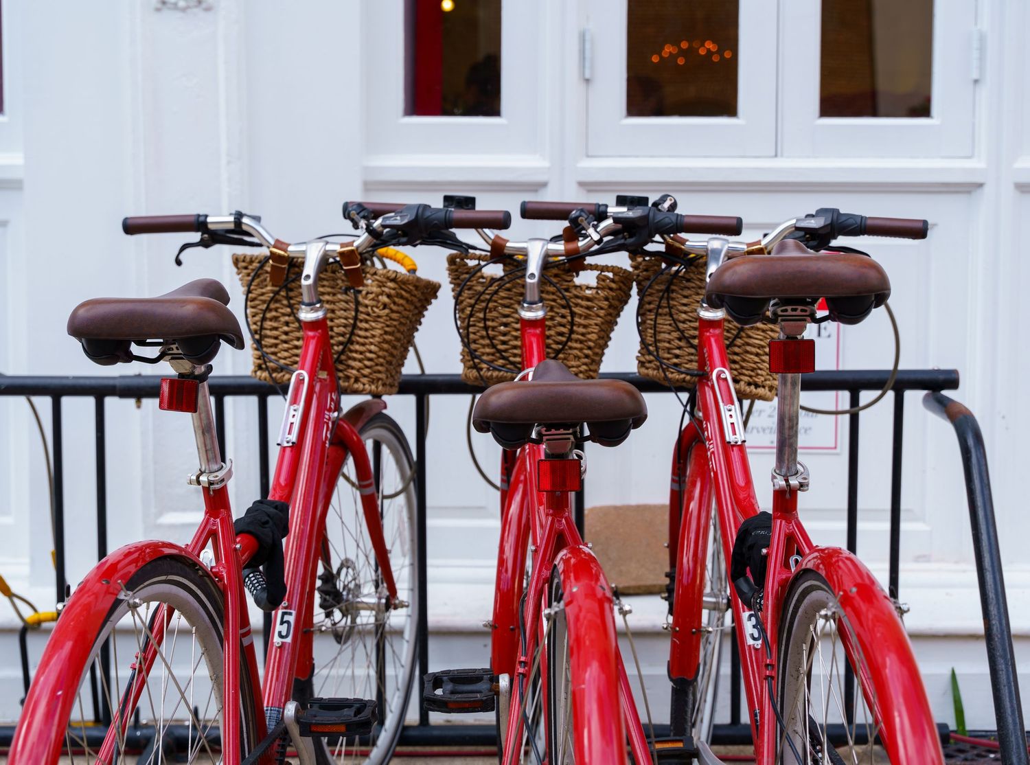 Row of red rental bikes parked in a line against a white building exterior.