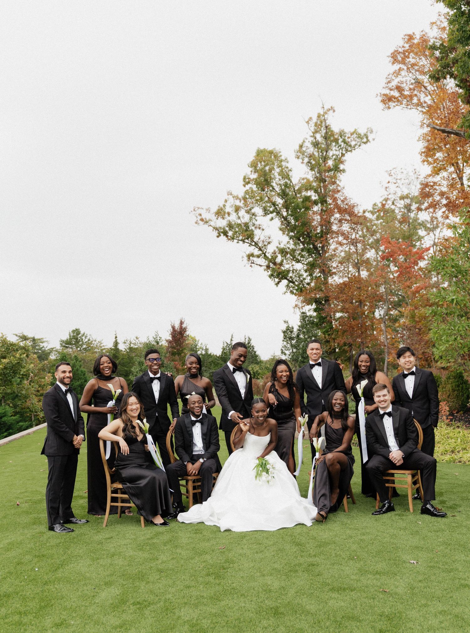 Newlyweds pose on deck overlooking autumn forest landscape in formal wedding attire.