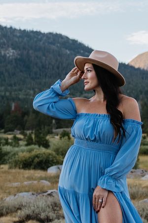 A pregnant woman wearing a blue sun dress and a tan cowboy hat looks out towards the Sierra's near Lake Tahoe during a maternity photo shoot