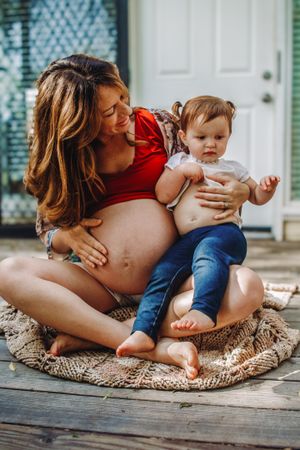 A pregnant mom and her 2-year old daughter each holds a hand to their bellies during a maternity photo shoot with Krystal Roina Photography.