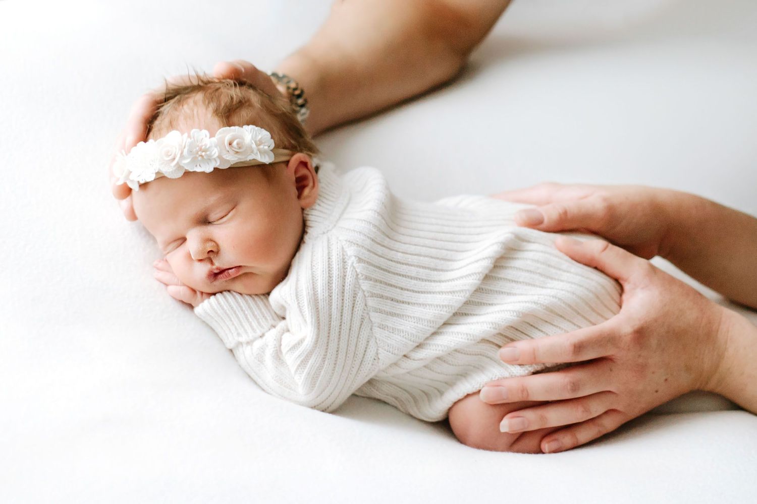 A sleeping newborn baby with soft delicate features wrapped in a white blanket, captured close up.