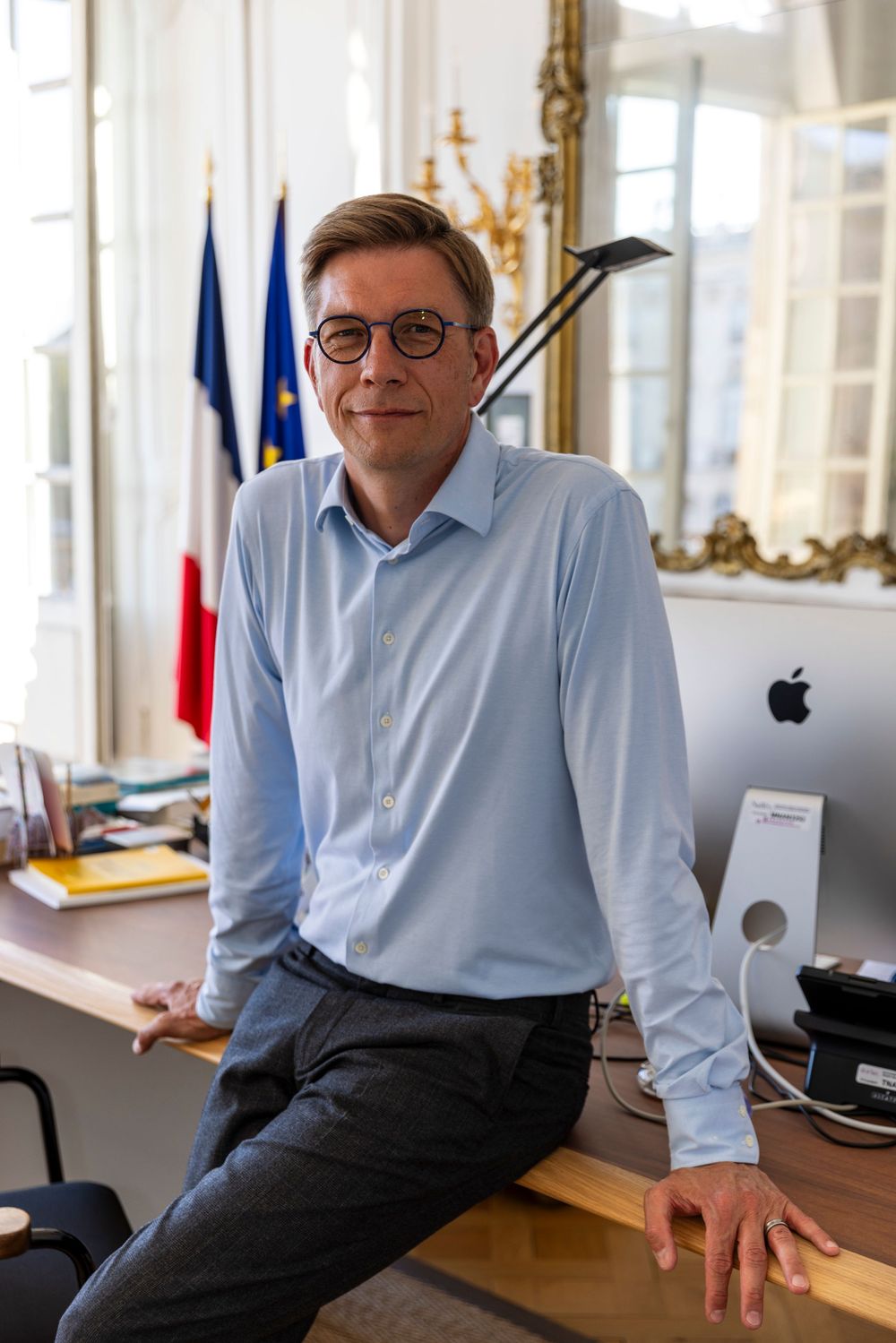 Professional at work in office with French flags and Apple computer workstation setup.