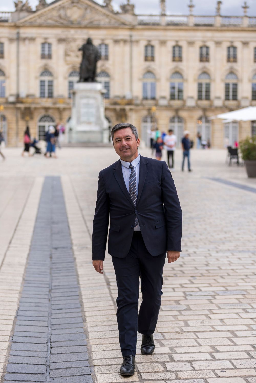 Person in dark business suit walking along stone path in front of historic European palace building.