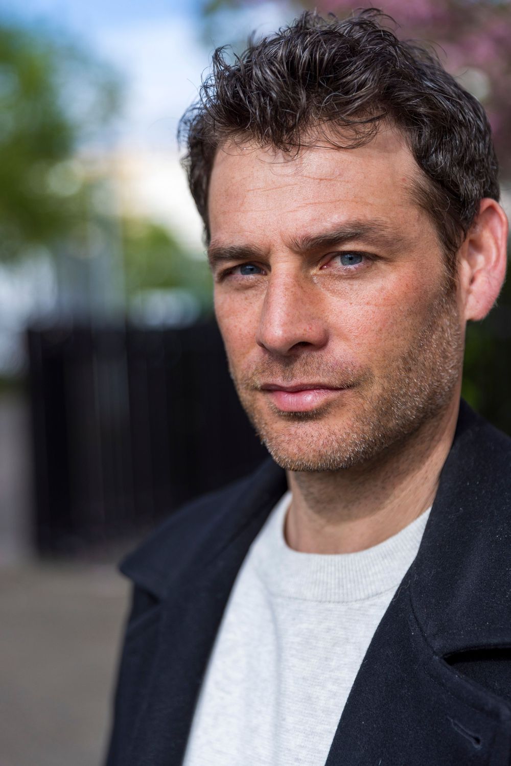 Portrait of person in casual attire against blurred outdoor background.