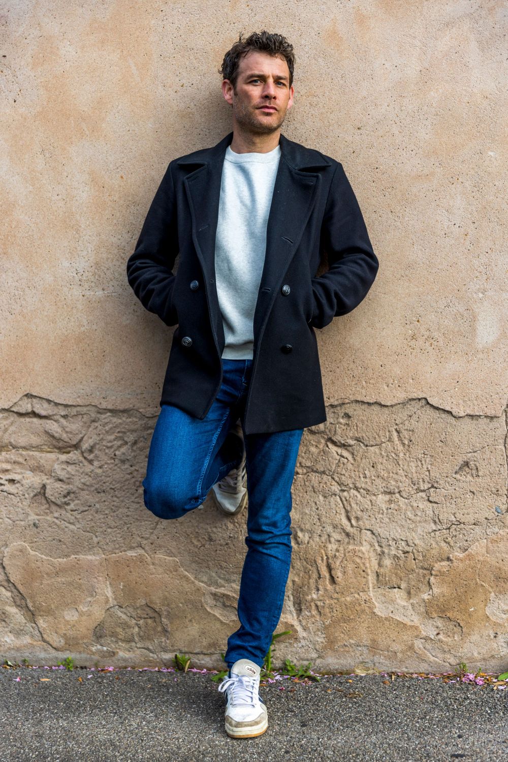 Casual street fashion portrait against textured beige wall.