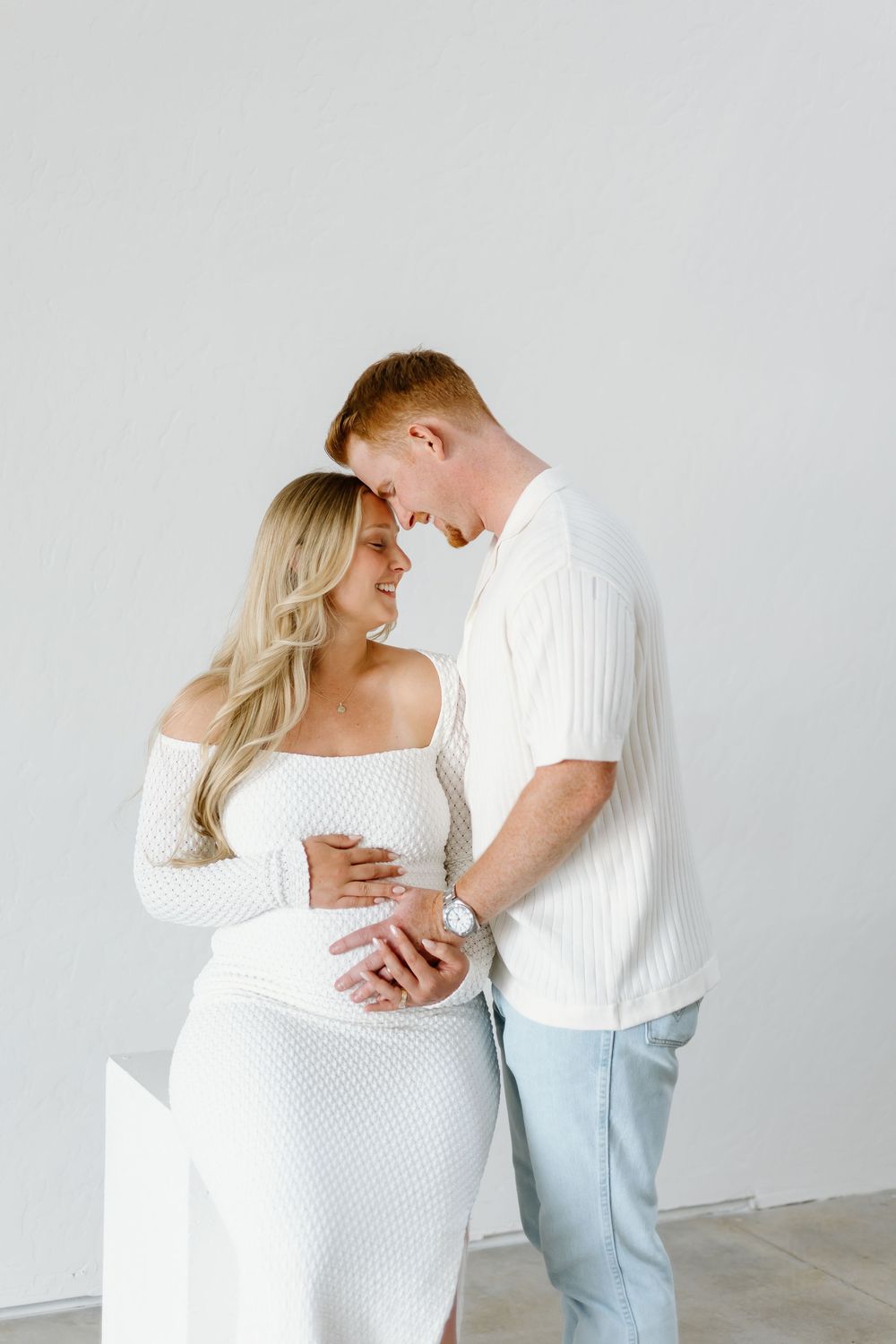 A series of intimate maternity photos showing a couple in white clothing against a light background.
