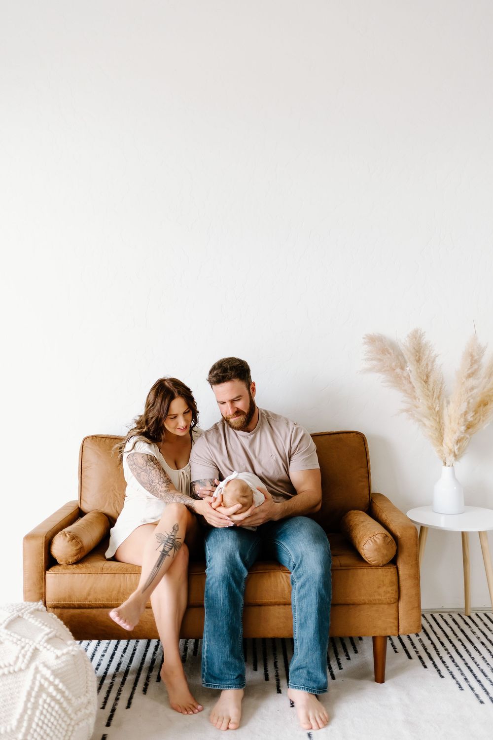 Couple lounges together on a tan couch in a minimalist room with pampas grass decor.