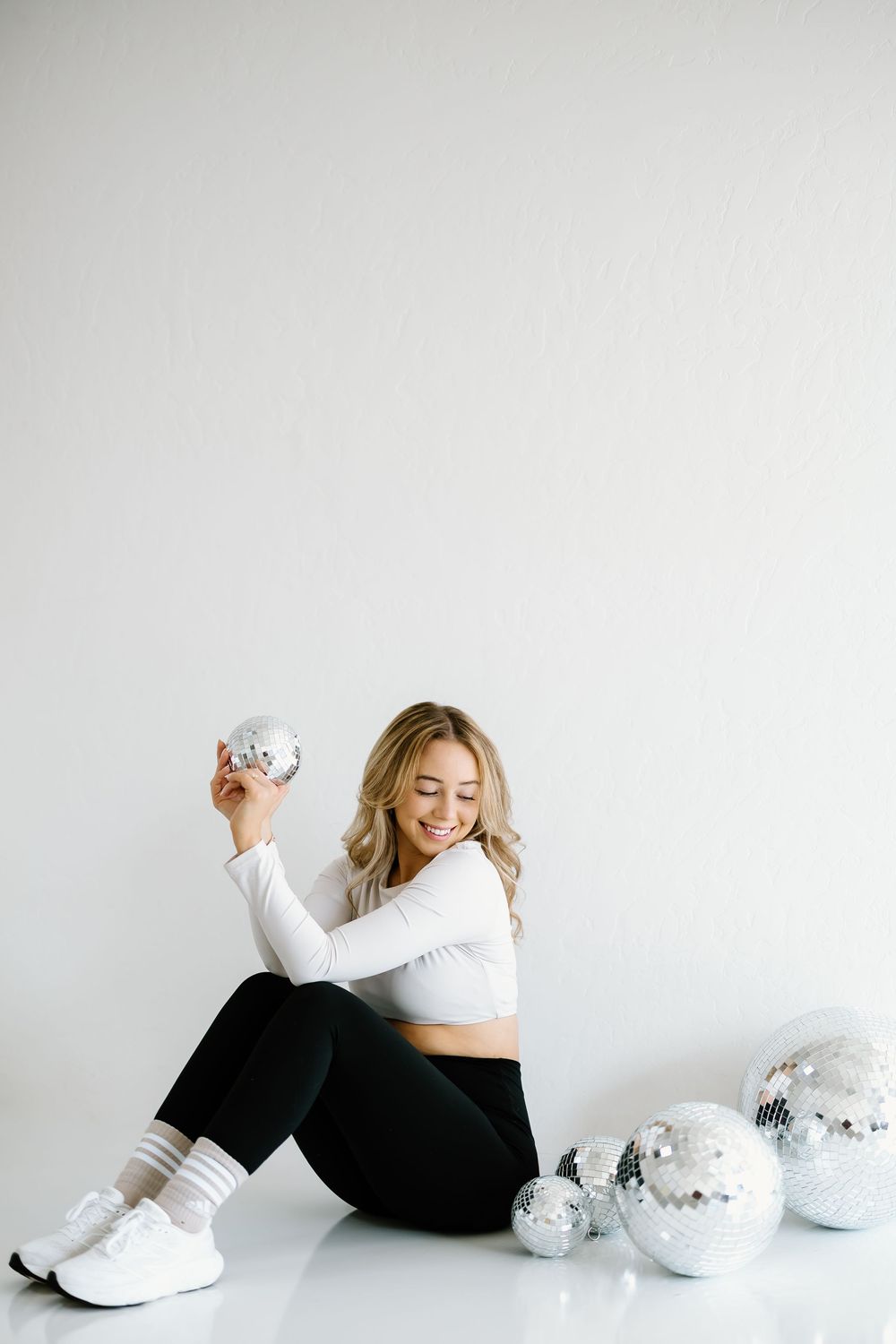 A woman in white lounges on the floor with decorative silver ornaments in a minimalist setting.