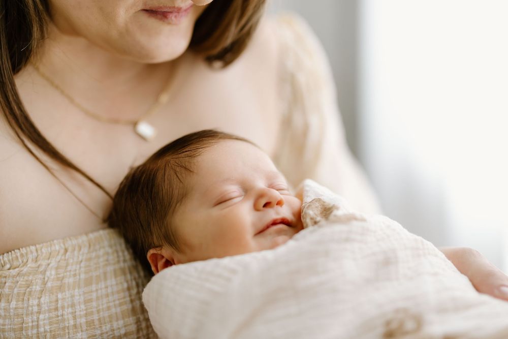 A newborn baby sleeps peacefully while swaddled in white blankets during a professional photo session.