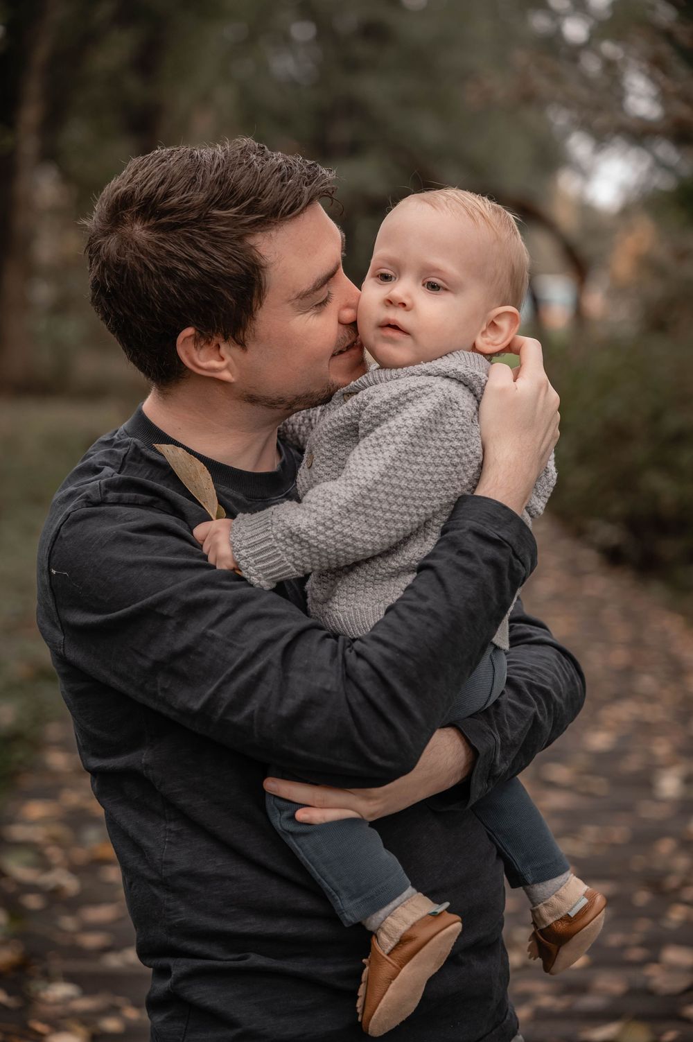 A touching sequence of a parent in a dark jacket sharing tender moments with a baby wearing a gray sweater outdoors.