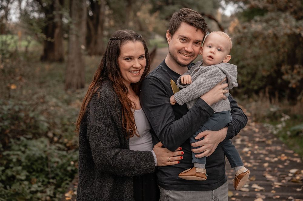 A family enjoys a playful autumn photoshoot together on a leaf-covered path in a wooded area.
