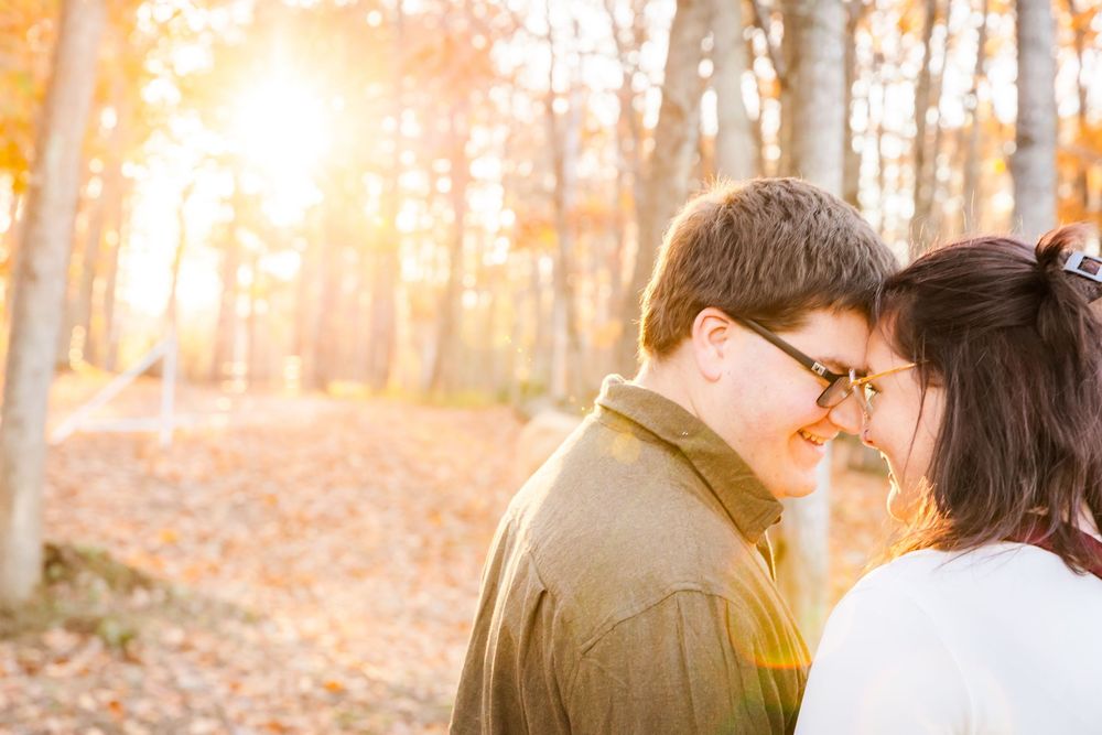 Intimate couple shares tender moment in sunlit autumn forest with golden light filtering through trees.