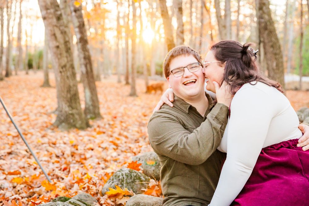 A loving autumn photo session in the woods with fallen orange leaves and golden sunlight filtering through the trees.