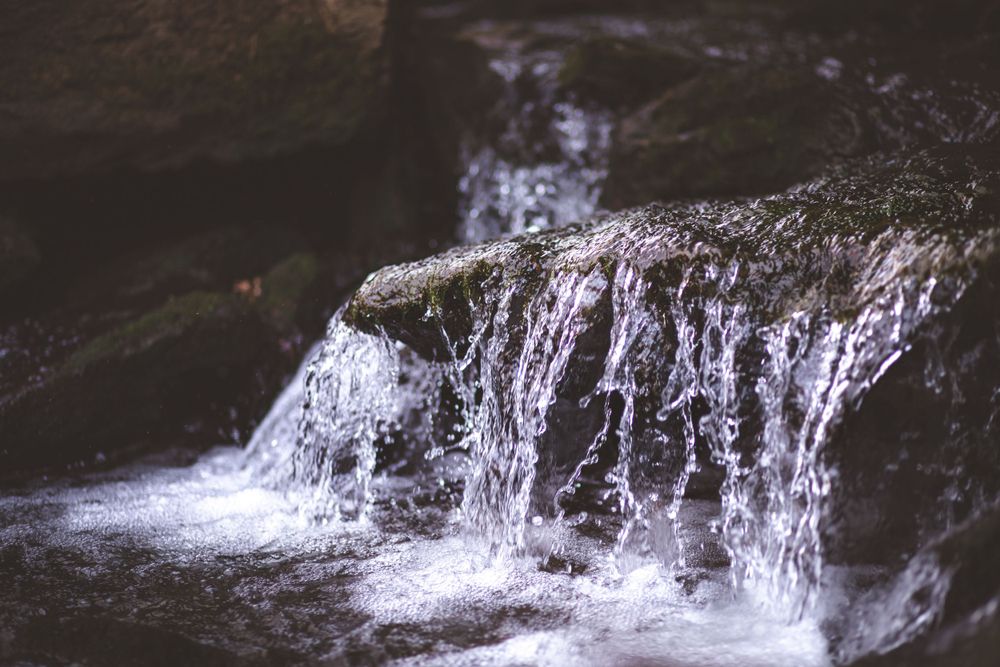 Crystal clear water cascades over dark rocks creating a small waterfall.