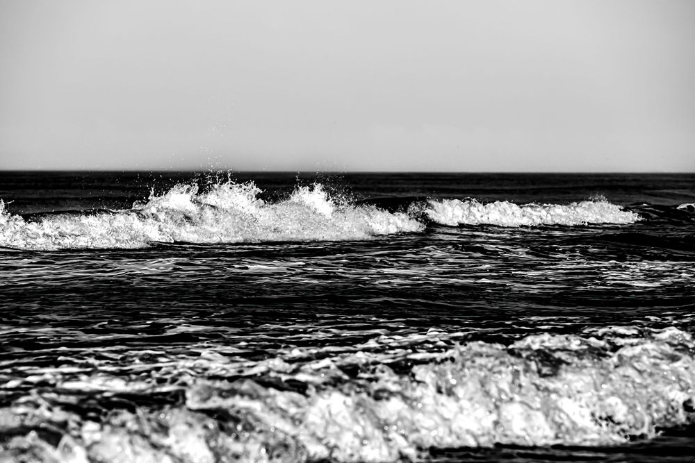 Black and white photograph of powerful ocean waves crashing with white foam spray.