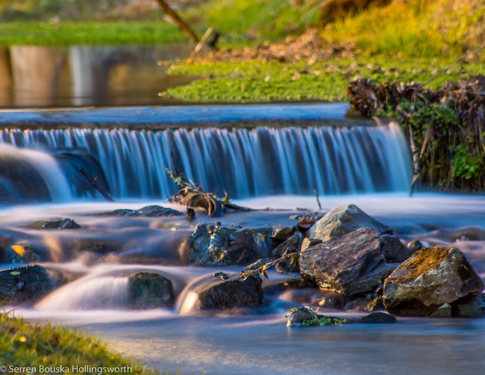 Small waterfall cascades over rocks creating smooth water motion effect in a natural setting.