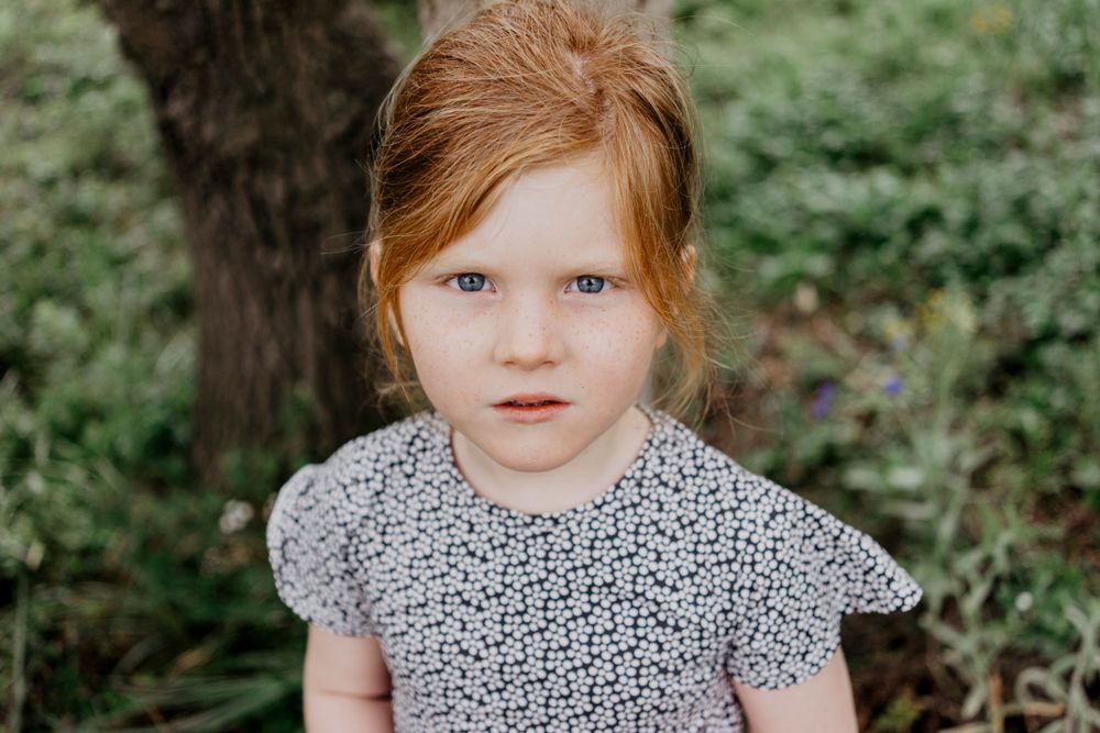 Retrato de uma menina com expressão serena,cercada por galhos ao ar livre, transmitindo naturalidade e doçura infantil em ambiente campestre