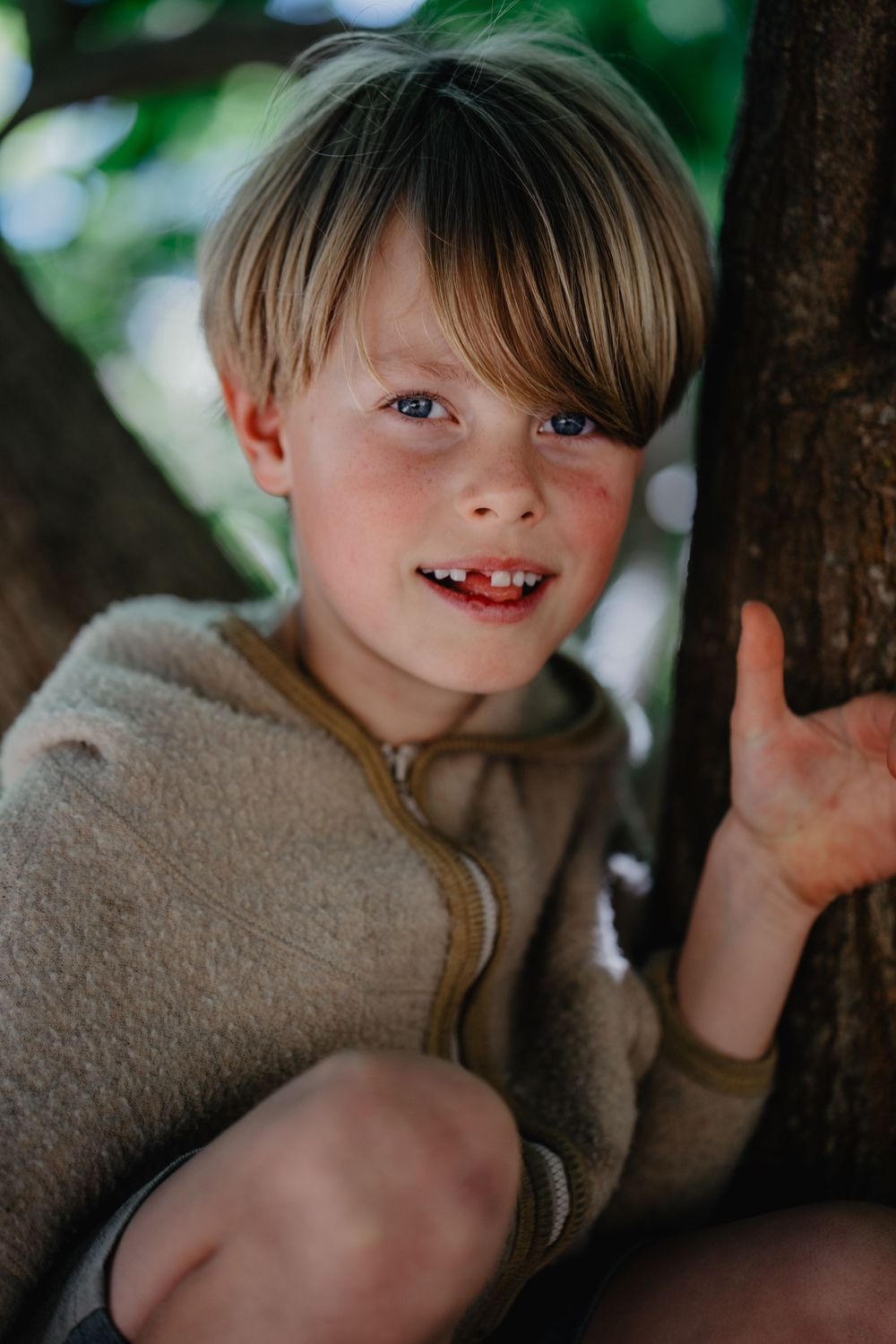 Retrato de uma menino com expressão serena,cercada por galhos ao ar livre, transmitindo naturalidade e doçura infantil em ambiente campestre