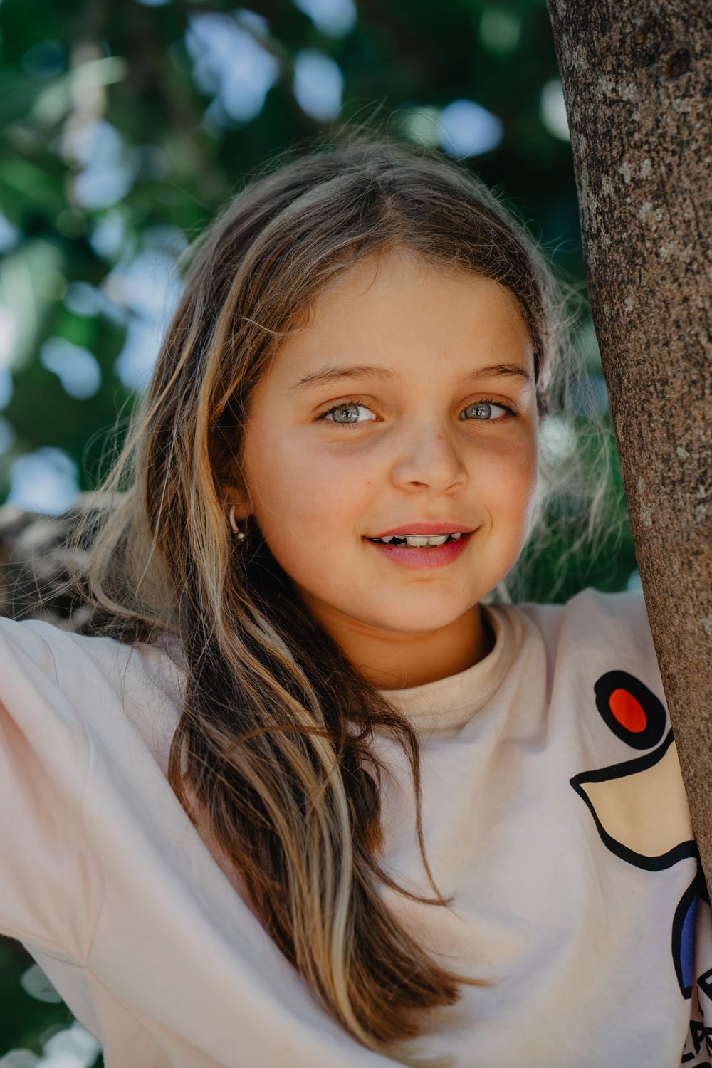 Retrato de uma menina com expressão serena,cercada por galhos ao ar livre, transmitindo naturalidade e doçura infantil em ambiente campestre