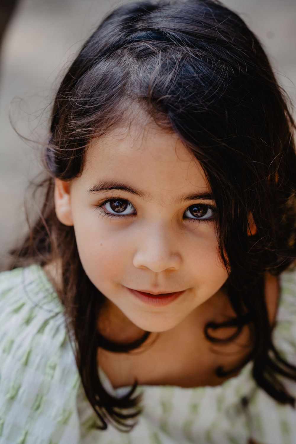 Retrato de uma menina com expressão serena,cercada por galhos ao ar livre, transmitindo naturalidade e doçura infantil em ambiente campestre