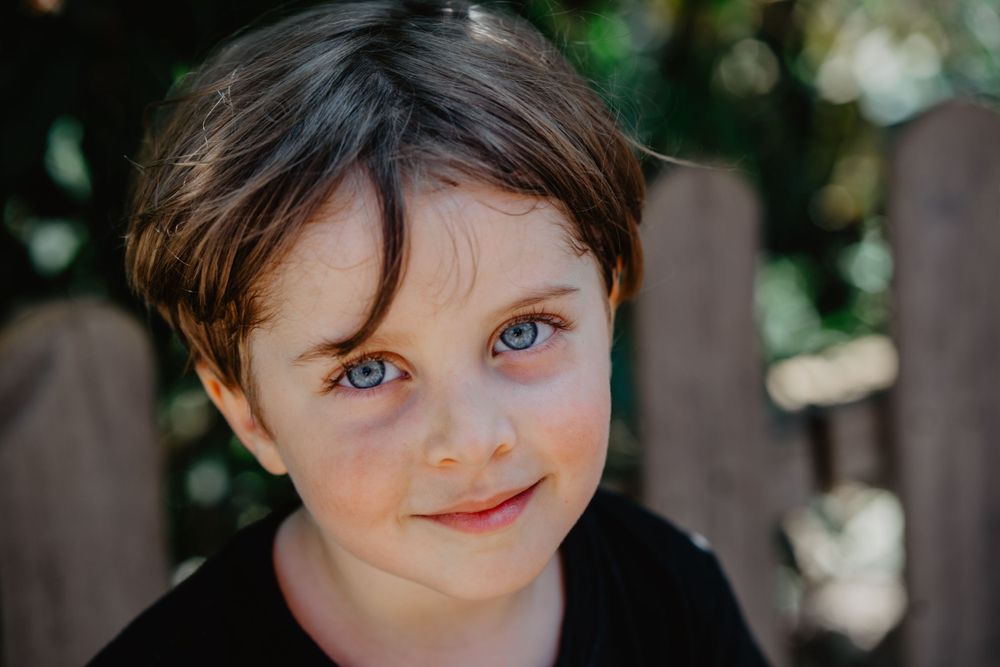 Retrato de uma menino com expressão serena,cercada por galhos ao ar livre, transmitindo naturalidade e doçura infantil em ambiente campestre