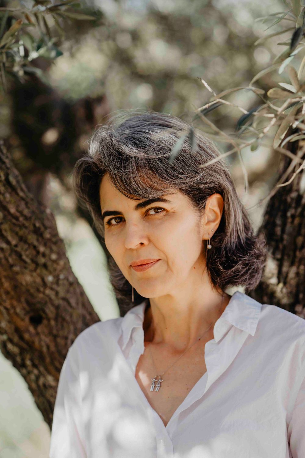 Retrato de uma mulher com expressão serena,cercada por galhos ao ar livre, transmitindo naturalidade e doçura infantil em ambiente campestre