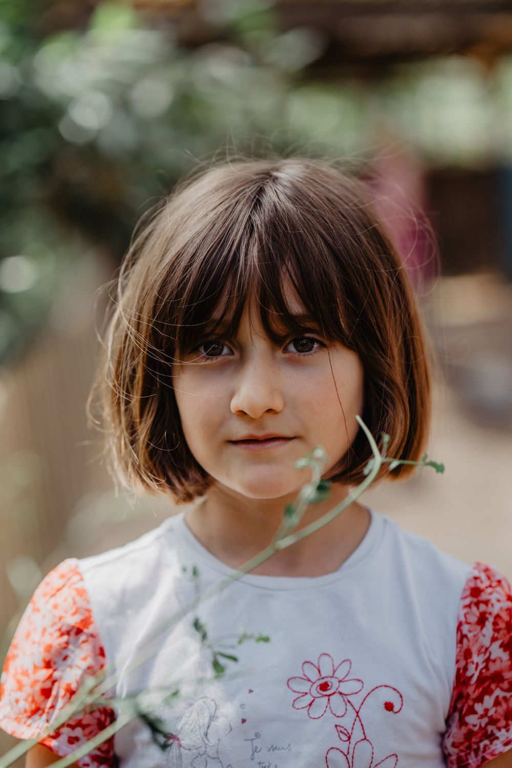 Retrato de uma menina com expressão serena,cercada por galhos ao ar livre, transmitindo naturalidade e doçura infantil em ambiente campestre