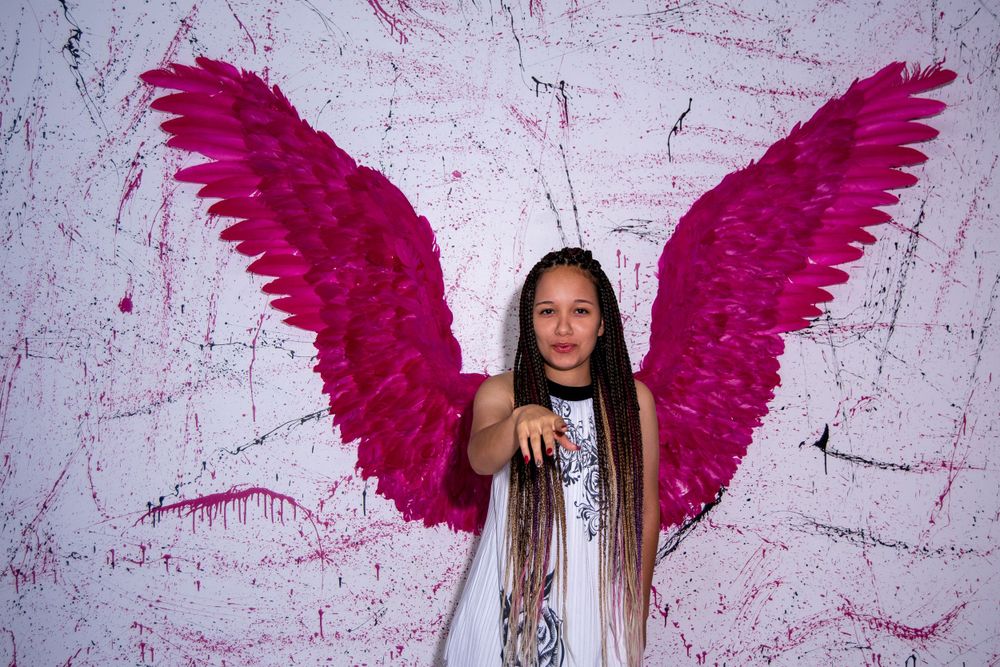 Figure with bright pink wings poses against white textured background.