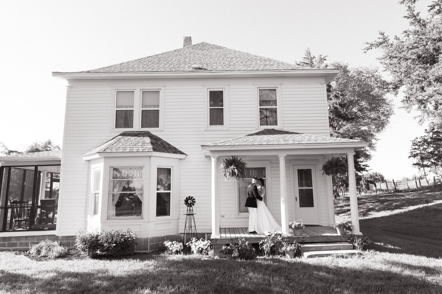 Classic white two-story farmhouse with wrap-around porch captured in black and white.