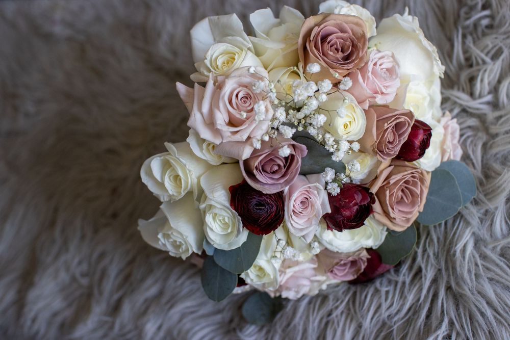 Bridal bouquet featuring white, blush, and deep red roses with baby's breath on a fur surface.