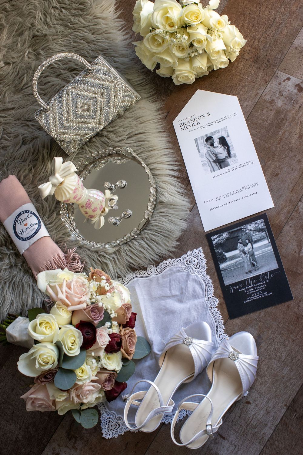 Flat lay of wedding details including bouquet, white heels, invitation suite, jewelry, and beaded clutch.