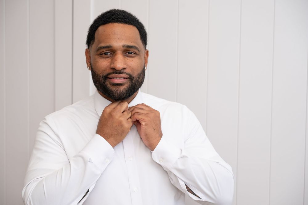 Handsome Black man in white dress shirt adjusting collar against white background.
