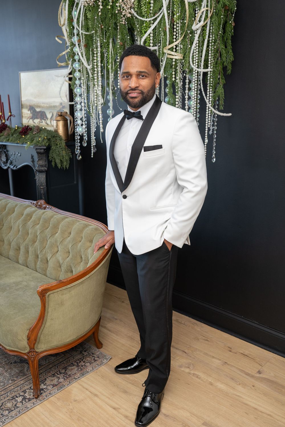 Groom in white tuxedo jacket with black lapels posing in elegantly decorated indoor setting.
