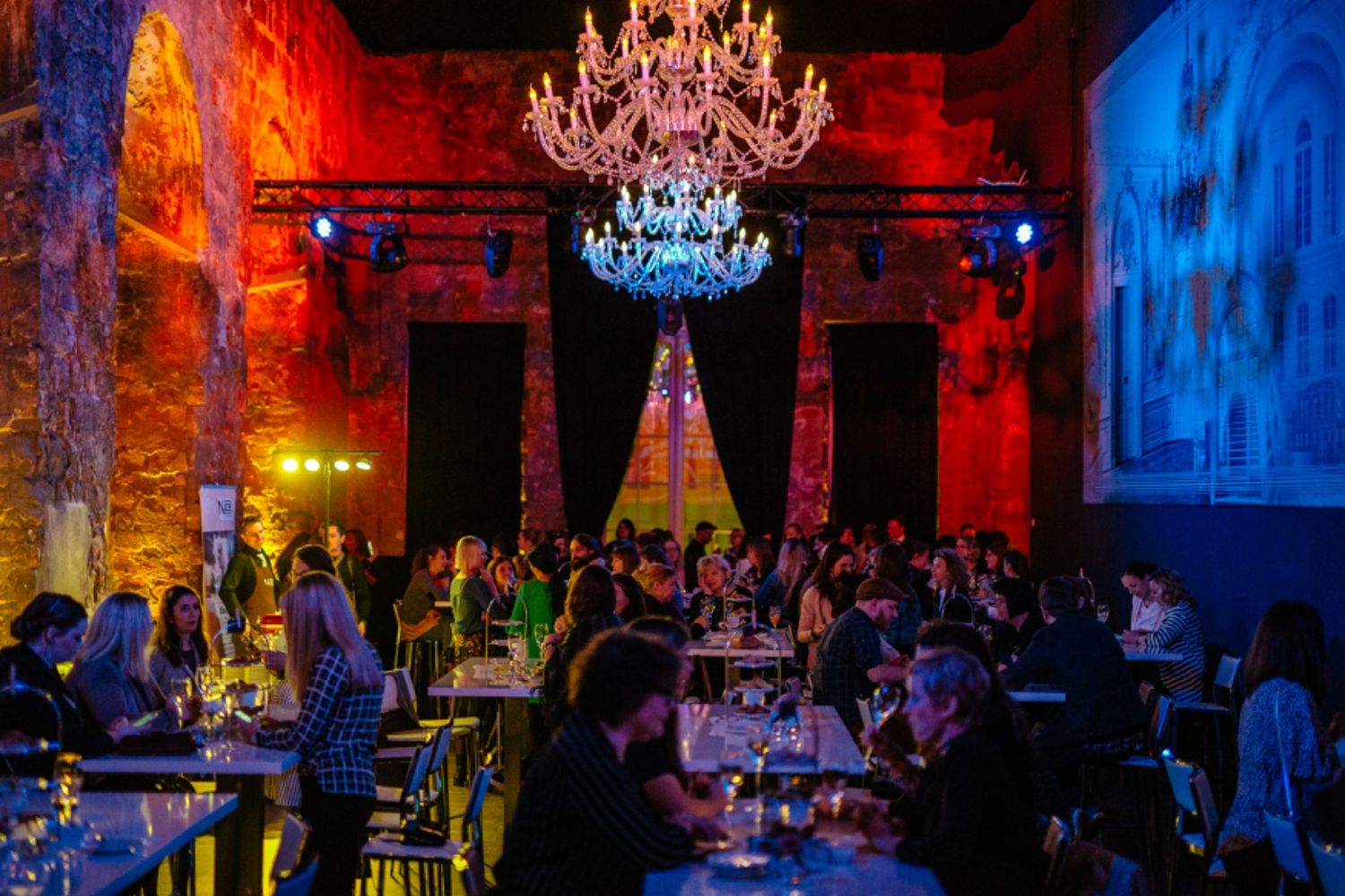 Elegant chandelier illuminates a vibrant venue interior with dramatic red and blue lighting as patrons enjoy the atmosphere.